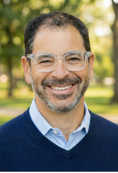 Headshot of a man with clear glasses in a blue sweater smiling for a photo.