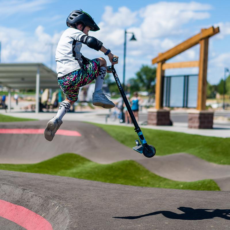 Kid does jump on scooter on pump track. 