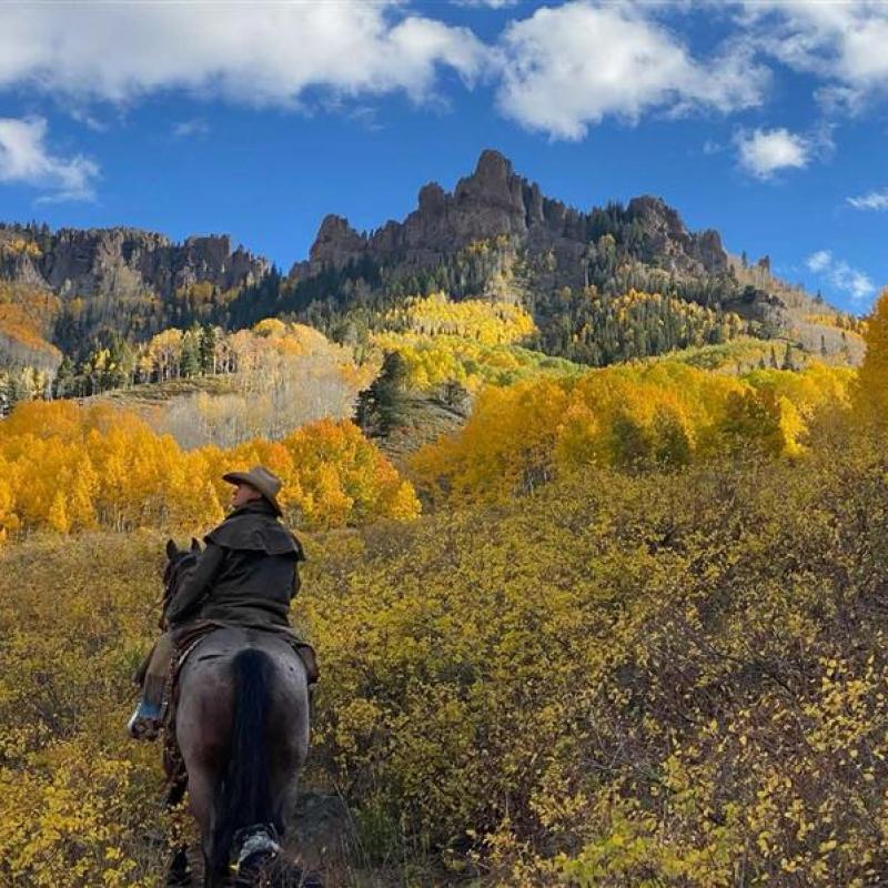 Man riding his horse in the wilderness, with a mountain backdrop in autumn colors. 