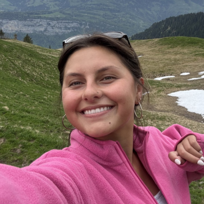 Sofia in a pink sweater posing for a photo with a mountain backdrop. 