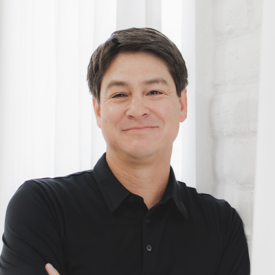 Headshot of Ray Rivera posing for a photo with his arms crossed, wearing a black shirt against a white backdrop. 