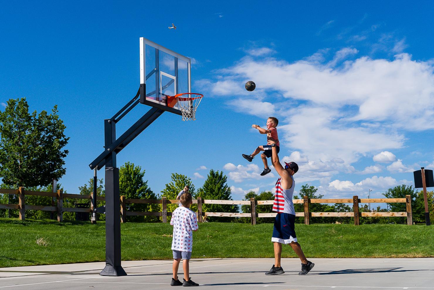 Parent holds child up to shoot a basketball into the hoop. 