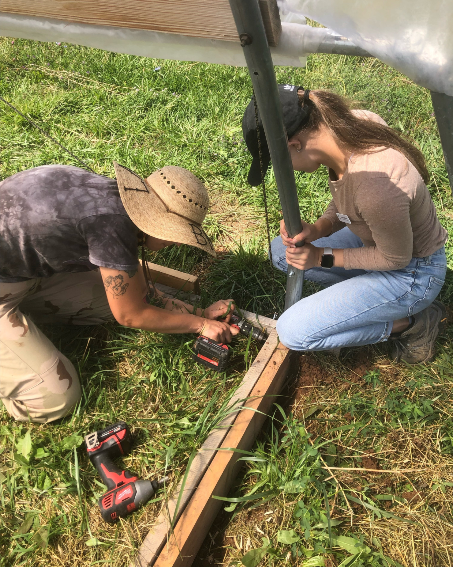 Two people helping build a structure with wood and metal outside. Taken from above