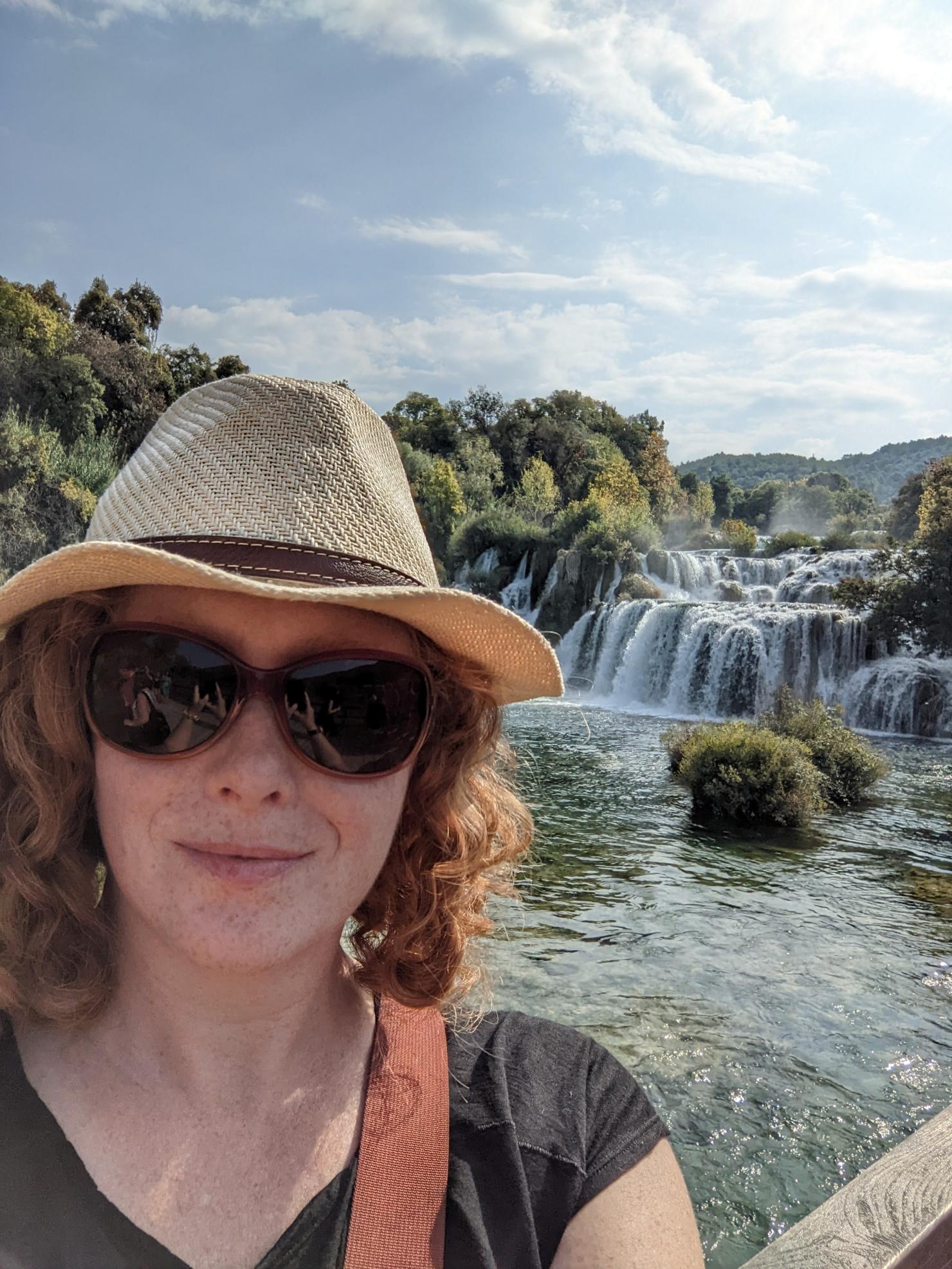 Amber Shanklin posing for a selfie with gorgeous waterfall scenery in the backround.
