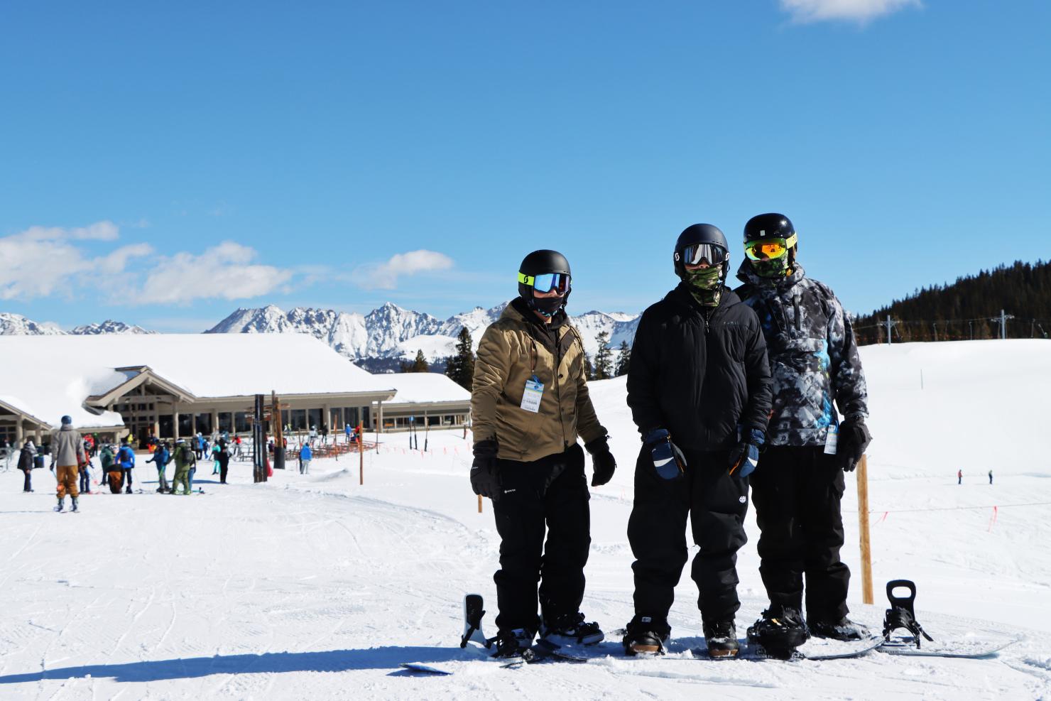 Three people in snowboard gear on a snowy hill posing for a photo. 