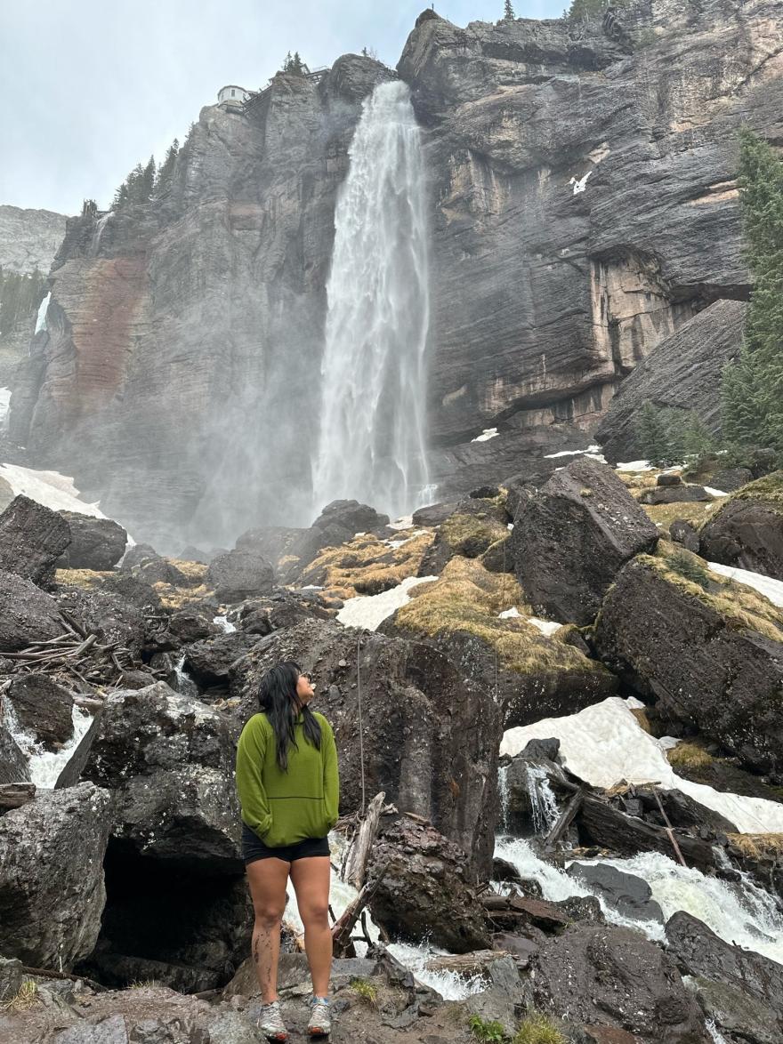 Andrea Torres looking back at a waterfall scene behind her. 