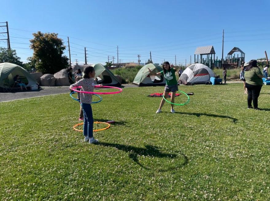 Kids hoola hooping in a green field with tents in the background. 