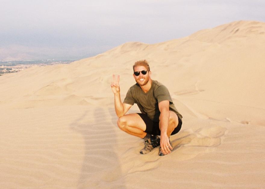 Payton kneeling down posing for a photo on what appears to be sand dunes. 