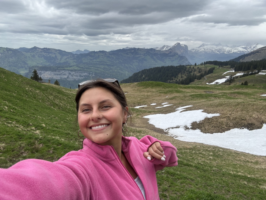 Sofia Blanco posing for a selfie in a pink sweater with a mountain backdrop.